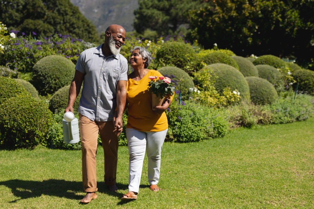 Senior african american couple spending time in sunny garden together walking and smiling.