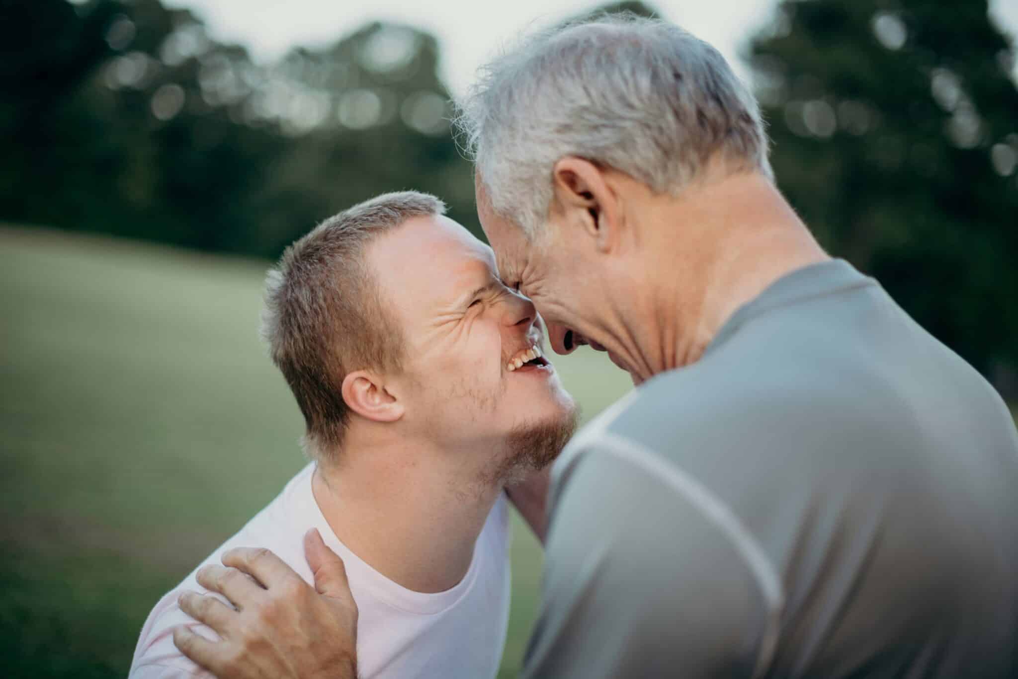 father and special needs son stand smiling with their faces touching
