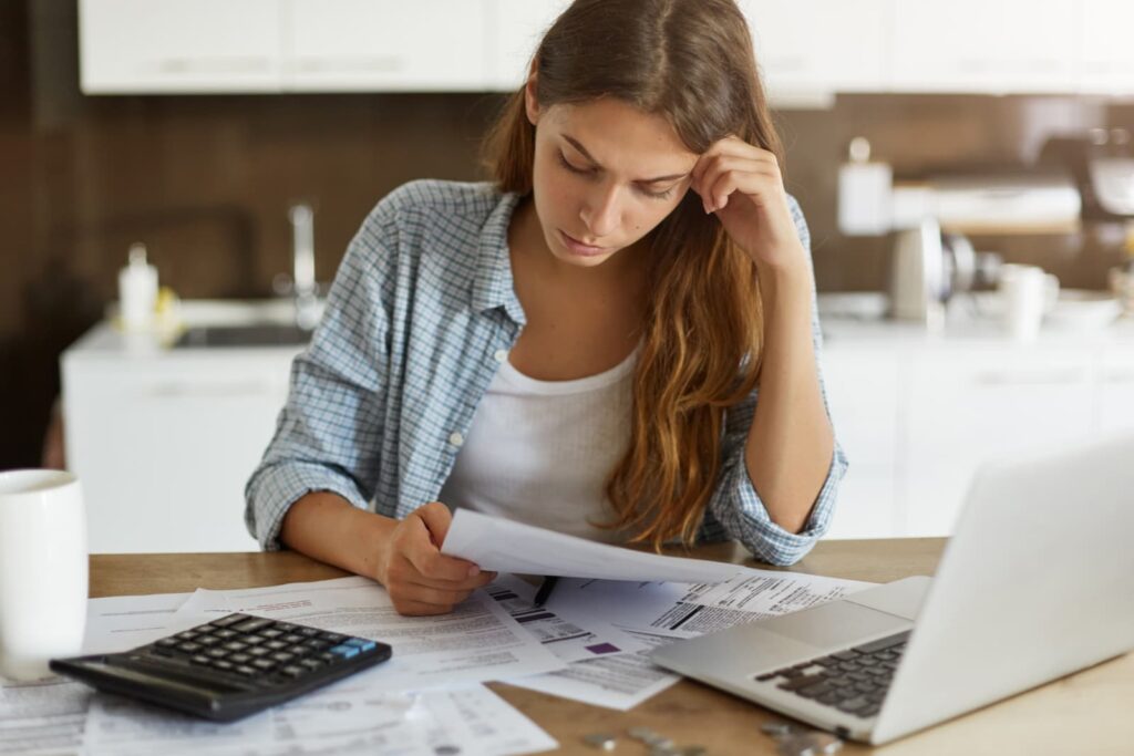 woman sits at kitchen table looking at bills